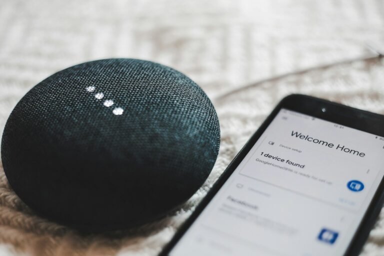 Charcoal smart speaker with glowing lights next to a smartphone, illustrating AI voice assistants